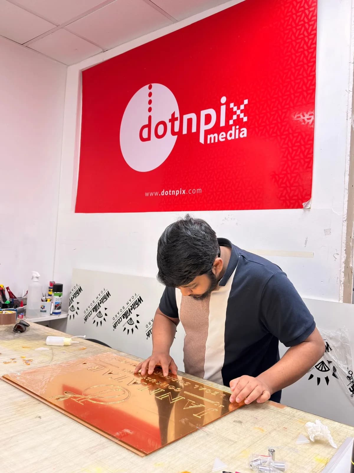 A gold-lettered plaque being checked by hand on the studio bench